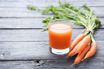 Fresh carrot with glass of juice on grey wooden table