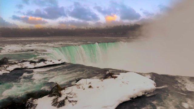 Drone flies over the edge of Niagara Falls at sunset.
