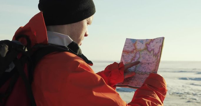 Man hiker is looking at the map in snow mountains checking the route. Winter travel hiking. Back view.