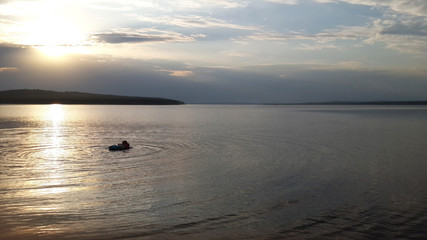 the girl with oversleeves for swimming on hands floats down the river holding a rubber ring against the background of the sunset sun