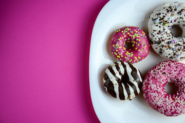 Fototapeta na wymiar Assorted donuts with chocolate frosted, pink glazed and sprinkles donuts. Pink pastel background. Copy space for text. Horizontal.