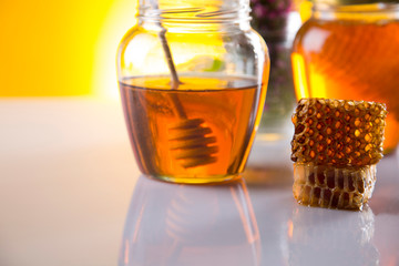 Honey dripping from a wooden honey dipper in a jar on wooden background