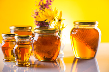 Honey dripping from a wooden honey dipper in a jar on wooden background