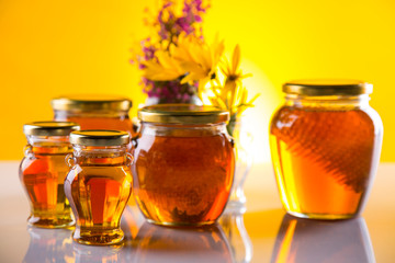 Honey dripping from a wooden honey dipper in a jar on wooden background