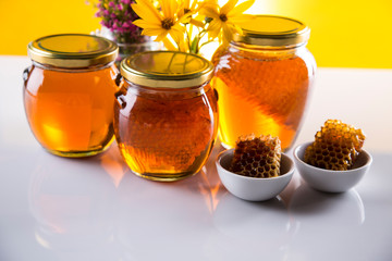 Honey dripping from a wooden honey dipper in a jar on wooden background