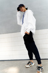 Asian girl weaing a large white hoodle under a clean background, black pants and sports shoes