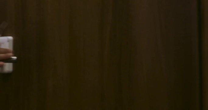 Man comes to the door of the hotel and opens room using an electronic key card. Enters the room and closes the door. Hand close-up, side view.
