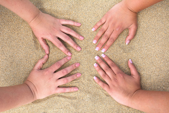 Four female hands placed on the beach sand.