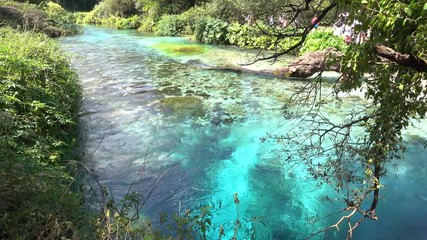 Countless tourists walk along the breathtaking turquoise colored river running through the picturesque national park in Albania. Cold fresh spring water comes bubbling out of the famous Blue Eye well