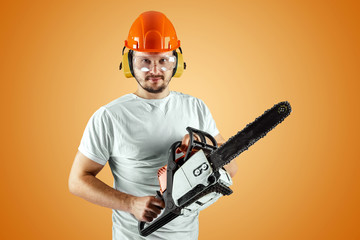 Bearded man in a helmet holds a chainsaw on an orange background. Construction concept, contractor, repair, lumberjack.