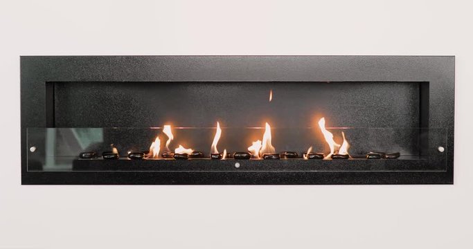 Decorative artificial fireplace with black stones in room interior in white wall. Close-up fireplace, front view.