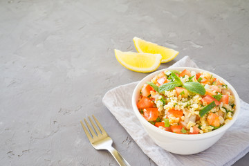 Tabbouleh salad with bulgur, parsley, mint  and tomato in a white bowl on a gray concrete background with copy space for text. Traditional Lebanese Arabic Salad