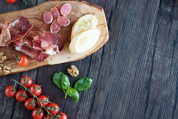 Prosciutto, bread, olives, walnut, mozzarella, salami, basil and cherry tomatoes on  brown wooden board.  Mediterranean kitchen. Top view.