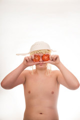 A young, fat, cheerful, smiling boy with tomatoes and a colander and spaghetti noodles on his head. Plump body without clothing. White background. Portrait photo.