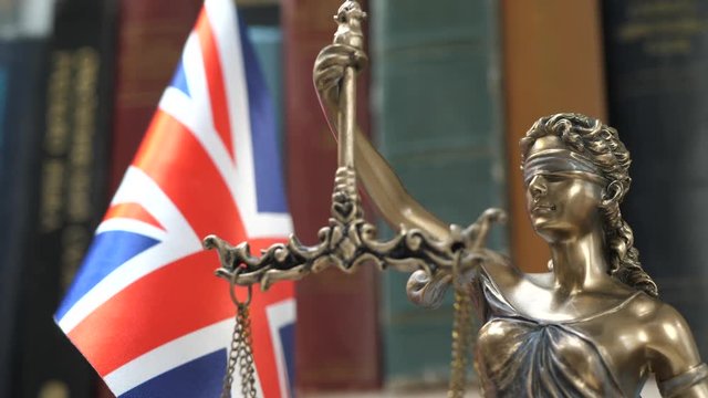 Statue of Lady Justice with Bookshelf with Books and United Kingdom Flag Background. Tribunal and justice concept. Consultation with insurance lawyer and customer