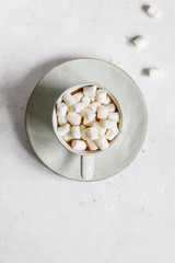 Hot chocolate with marshmallow in a ceramic mug over textured white background. Minimalist style, top view, copy space.