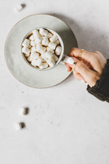 Girl's hand holds a cup of hot chocolate with marshmallow over textured white background. Minimalist style, top view, copy space.