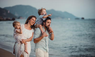 A young family with two toddler children standing on beach on summer holiday.