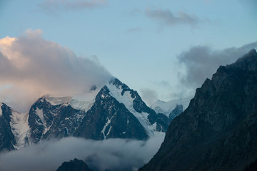 Low cloud before huge glacier. Giant snowy rocky mountains under cloudy sky. Thick mist in mountains at early morning. Impenetrable fog. Cold rocks. Dark atmospheric landscape. Tranquil atmosphere.