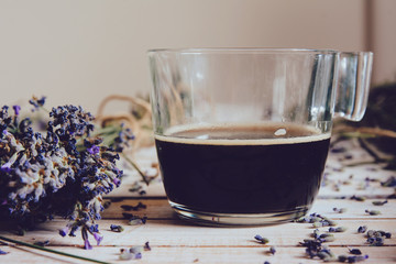 Cup of coffee and fresh lavender flowers, on wooden table.