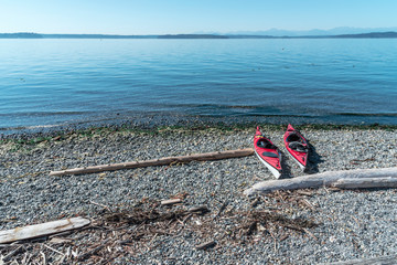 Two red kayaks resting on driftwood beach