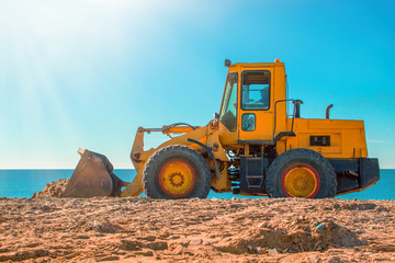 Yellow bulldozer on the background of clear blue sky and seashore. Lanscape and transport. Close up