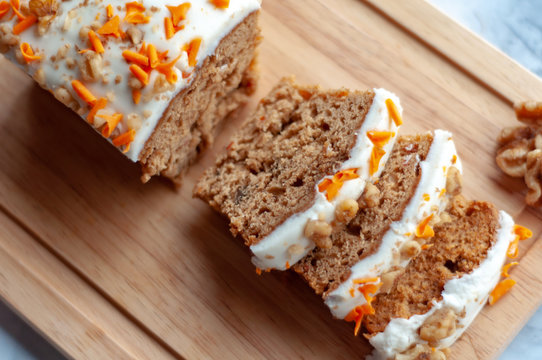 Loaf of carrot cake with cream cheese frosting and candy garnish on wooden table