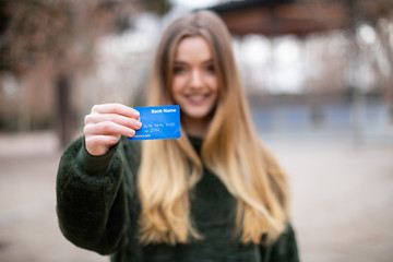 Happy young lady with credit card while standing in park