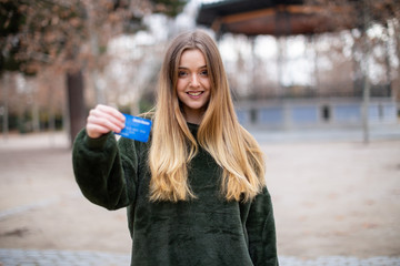 Happy young lady with credit card while standing in park