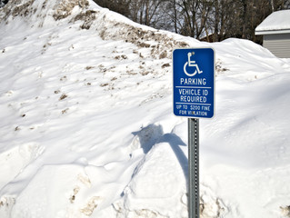 Handicapped parking sign in front of large pile snow parking lot in winter. © scandamerican