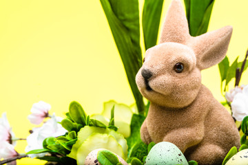 Easter bunny in decoration with eggs. Holiday card with yellow background.