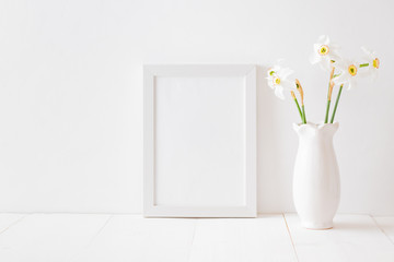 Mockup with a white frame and white daffodils in a vase on a white wooden table