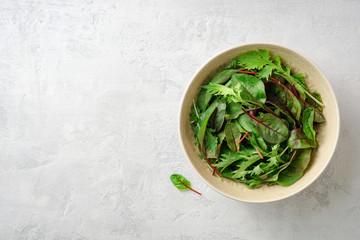 Fresh Chard and Mizuna leaves in bowl on gray concrete background. Top view. Copy space.