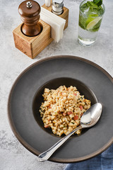 Barley porridge with chicken and bacon in a dark plate on a light table