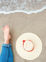 Feet of caucasian woman in jeans sitting by the sea on the coast with hat near by. Travel abstract photo