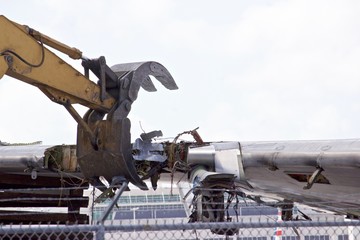 Aircraft wing section being reduced to scrap by a demolition excavator with a claw