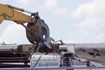 Aircraft wing section being reduced to scrap by a demolition excavator with a claw