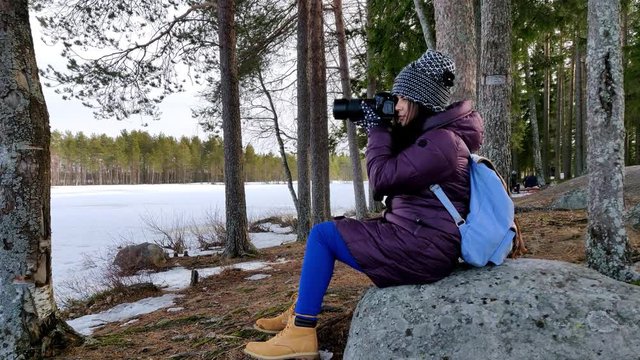 Thoughtful beautiful woman taking pictures in outdoor snow covered nature in a cold windy day in fast motion