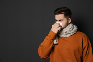Fototapeta premium Handsome young man blowing nose against dark background. Space for text