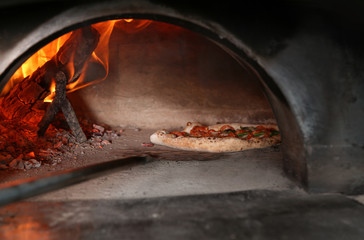 Taking out tasty pizza from oven in restaurant kitchen
