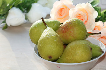 Pears with drops on a sunny table. A bouquet of cream roses in the background creates a good mood of a spring morning and a good day.