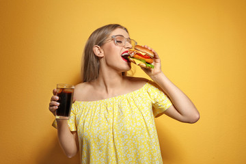 Pretty woman with tasty burger and cola on color background
