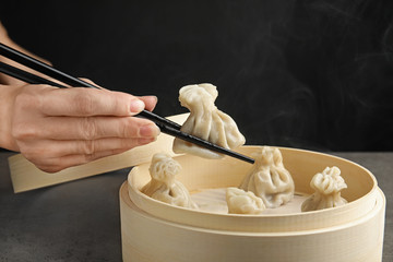 Woman cooking tasty baozi dumplings in bamboo steamer at table, closeup