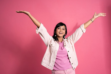 portrait of young woman raised arm happily over pink background
