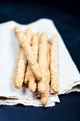 Italian grissini or salted bread sticks with sesame on linen napkin on black board background.