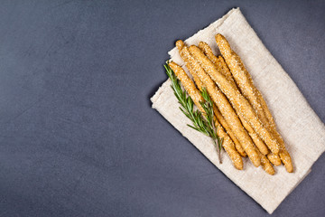 Italian grissini or salted bread sticks with sesame and rosemary herb on black board background.