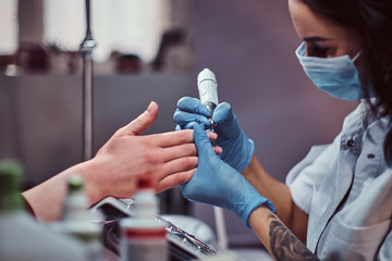 Beautician master in gloves applying nail drill to trim and remove cuticles. Hardware manicure in a beauty salon