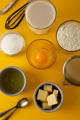 Obraz na płótnie Canvas Ingredients for baking pastry or dessert - butter, flour, eggs, milk, sugar. Yellow background, flat lay. Dessert recipe, cooking process. Copy space.