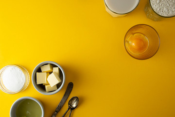 Ingredients frame for baking pastry or dessert - butter, flour, eggs, milk, sugar. Yellow background, flat lay. Dessert recipe, cooking process. Copy space.