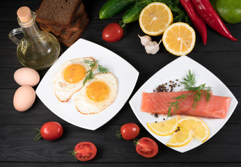 red fish, fried eggs with vegetables on a black wooden background